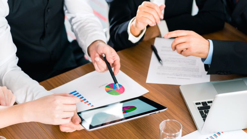 Hände von mehreren Business-Personen über einem Tisch mit Tablet  und Diagrammen