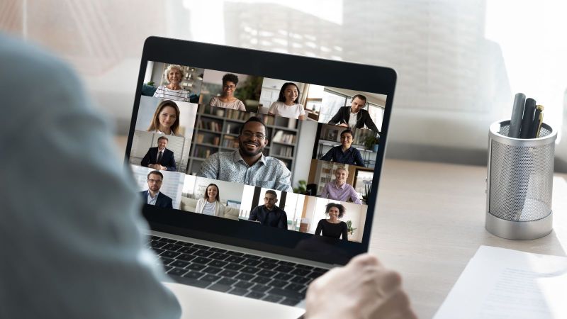 Rückansicht eines Mitarbeiters bei einer Webcam-Konferenz mit Kollegen.