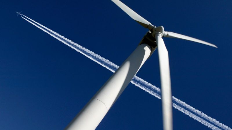 Flugzeug fliegt über einer Windenergieanlage.