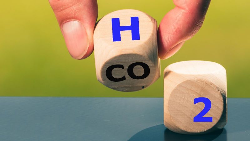 Eine Hand dreht einen Würfel, sodass anstatt CO2 die Buchstaben H2 zu sehen sind.