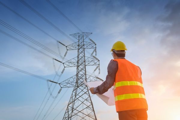 (Bild: ©Aunging - stock.adobe.com) Bauarbeiter steht vor Strommast
