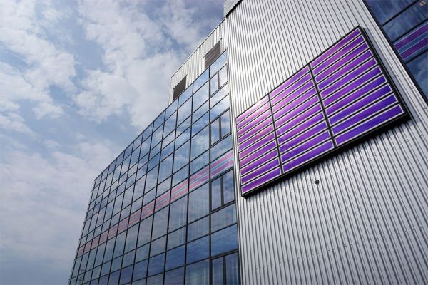 In die Fassade eines großen Gebäudes sind großflächige, blau scheinende Photovoltaik-Module integriert.