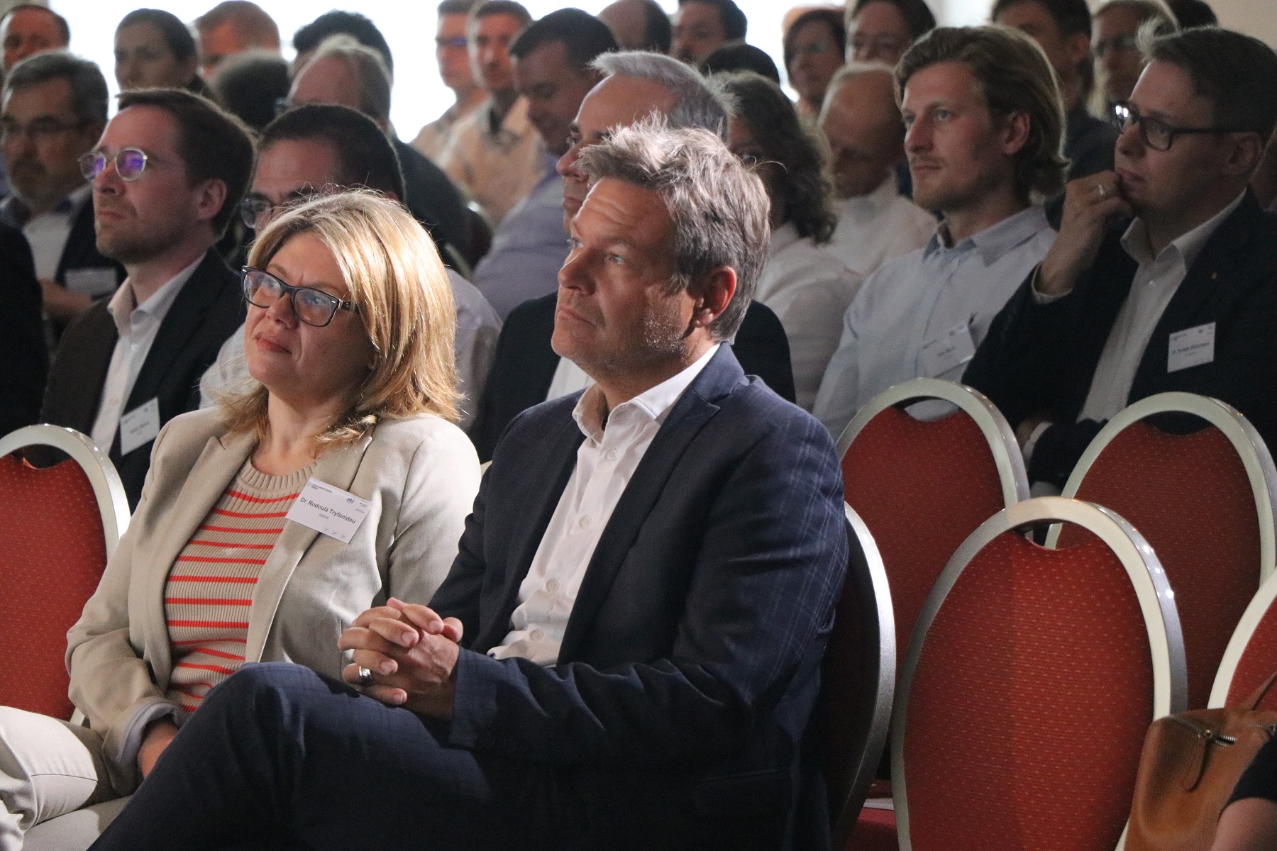 Rodoula Tryfonidou, Leiterin des Referats „Energieforschung – Grundsatzfragen und Strategie“, und Bundeswirtschaftsminister Robert Habeck folgen den Ausführungen auf dem Podium des Symposiums der Forschungsnetzwerke Energie.