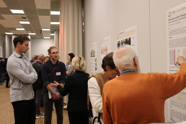 Mehrere Teilnehmende stehen während des Posterwalks in kleinen Gruppen vor wissenschaftlichen Postern. Sie betrachten die dargestellten Inhalte und diskutieren miteinander.