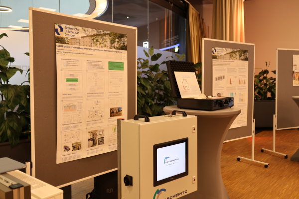 Projektstand von KUEHASystem mit zwei wissenschaftlichen Postern der Technischen Universität Dresden und einem technischen Demonstrator mit Bildschirm im Vordergrund.