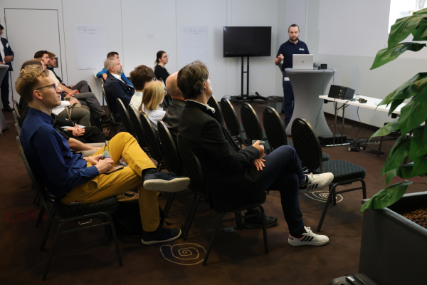 Teilnehmende eines Workshops sitzen vor einer Präsentationsfläche. Ein Referent steht am Rednerpult und erläutert einen fachlichen Inhalt.